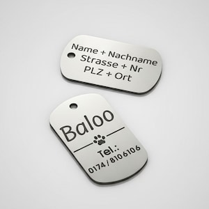 Könnte beinhalten: Zwei silberne Hundeanhänger mit abgerundeten Kanten. Ein Anhänger hat den Namen "Baloo" und einen Pfotenabdruck, darunter eine Telefonnummer. Der andere Anhänger hat Textzeilen.