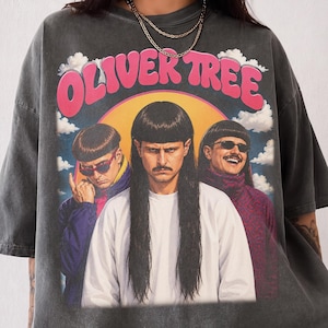 May include: A charcoal gray short-sleeve t-shirt featuring a graphic print of Oliver Tree with long hair and a mustache, flanked by two figures in sunglasses. The text OLIVER TREE appears in pink above the figures against a yellow sun and clouds.