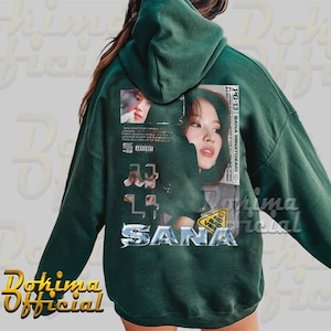 K&ouml;nnte beinhalten: Gr&uuml;ner Kapuzenpullover mit einem Grafikdruck eines Frauen Gesichts und dem Text "SANA" in einer silbernen Metallic-Schrift. Die Grafik enth&auml;lt auch den Text "PG-13" und "SANA MINATOZAKI".