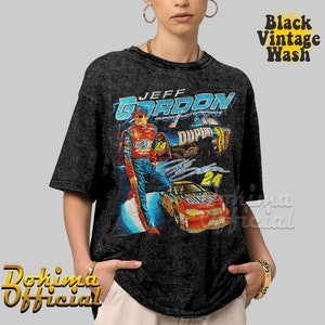 May include: Black vintage wash t-shirt featuring a graphic of Jeff Gordon, a race car driver, in a red race car with the text "JEFF GORDON" and "DUPONT MOTORSPORTS" on the shirt.