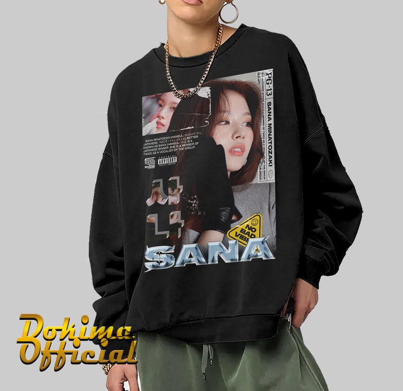 K&ouml;nnte beinhalten: Schwarzes Sweatshirt mit einem Grafikdruck eines Frauen Gesichts und dem Text "SANA MINATOZAKI" und "SANA". Die Grafik enth&auml;lt auch den Text "NO BAD VIBES" und ein gelbes Warnschild.