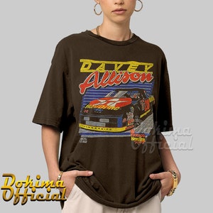 May include: Brown t-shirt with a vintage-style graphic of race car driver Davey Allison. The graphic features a red, white, and blue race car with the number 28 on the side. The text "Texaco Havoline Racing" is also visible on the graphic.
