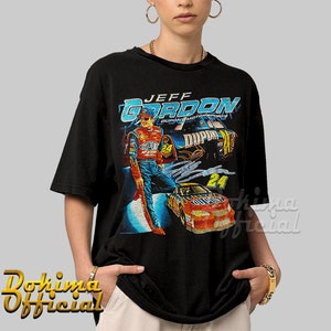 May include: Black t-shirt with a vintage-style graphic of race car driver Jeff Gordon, wearing a blue racing suit and a red helmet, standing next to his red race car with the number 24 on it. The text "JEFF GORDON" is printed in blue and white on the shirt.
