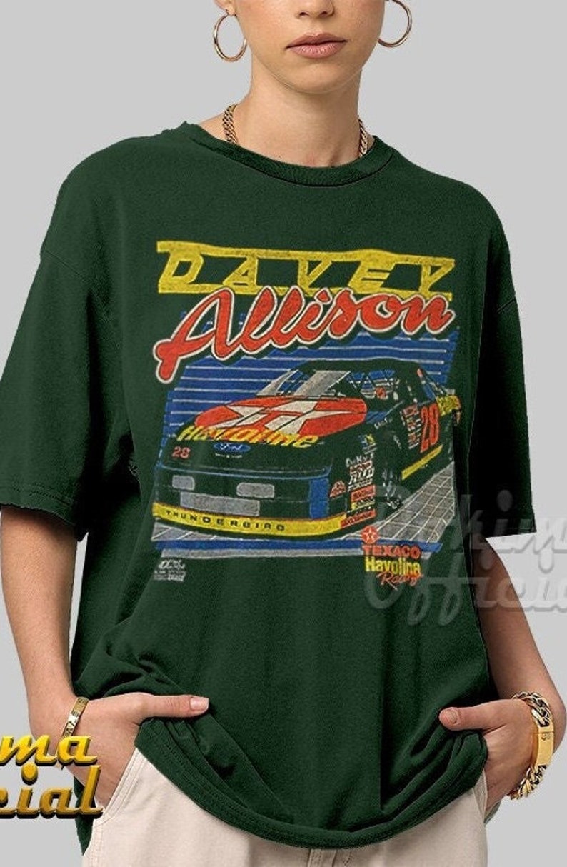 May include: A green t-shirt with a vintage-style graphic of race car driver Davey Allison. The graphic features a red, black, and white race car with the number 28 on the side. The text "Davey Allison" is in yellow and red lettering. The text "Texaco Havoline Racing" is also included in the graphic.