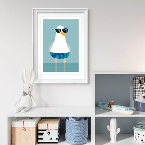 May include: Framed art print of a cartoon seagull wearing sunglasses and swimming trunks. The seagull is white with a yellow beak and blue and green patterned trunks. The background is a light blue.