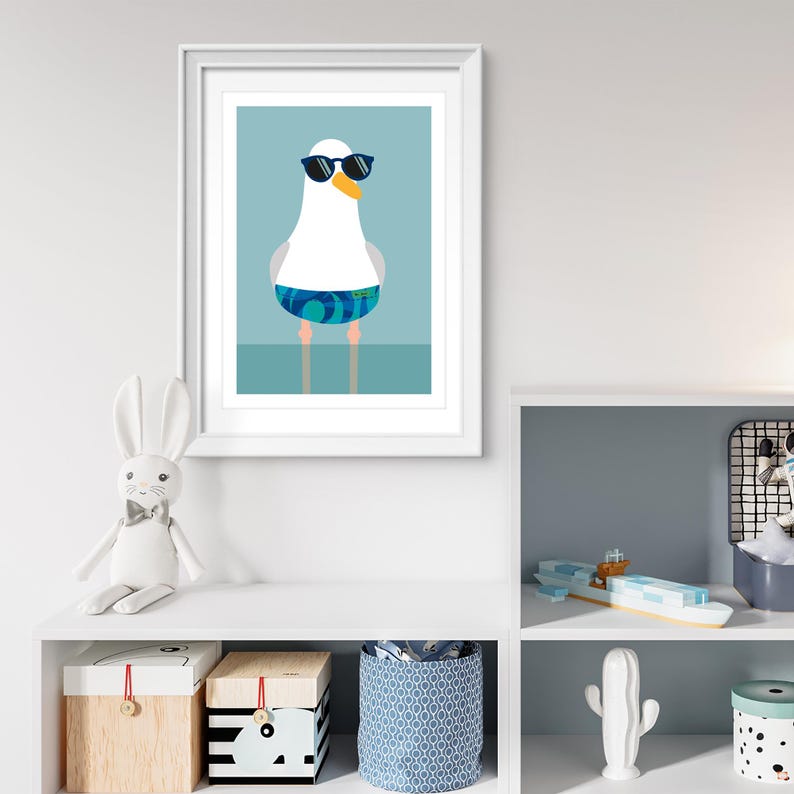 May include: Framed art print of a cartoon seagull wearing sunglasses and swimming trunks. The seagull is white with a yellow beak and blue and green patterned trunks. The background is a light blue.