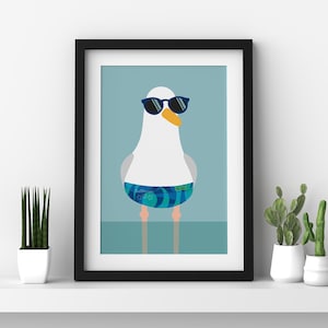 May include: Framed art print of a cartoon seagull wearing sunglasses and blue swim shorts. The seagull has a white body, grey wings, and an orange beak. The background is a light blue colour.