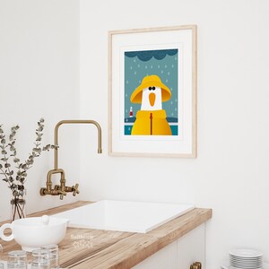 Peut inclure: Une illustration encadr&eacute;e d'une oie de dessin anim&eacute; portant un imperm&eacute;able et un chapeau jaunes, debout devant un phare sous la pluie. L'arri&egrave;re-plan est de couleur bleu-gris avec des gouttes de pluie blanches.