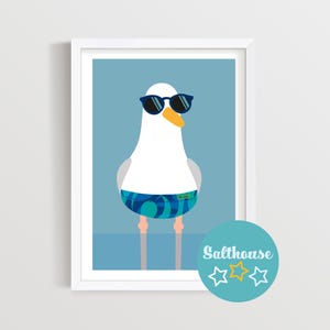 May include: A framed art print depicting a cartoon seagull in sunglasses and swimming trunks. The seagull is white with grey wings and an orange beak. The background is light blue. The print includes the text "Salthouse".