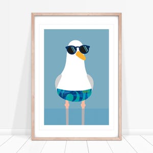 May include: A framed art print of a cartoon seagull wearing sunglasses and swim shorts. The seagull has a white body, grey wings, and an orange beak and legs. The background is light blue, and the seagull is wearing black sunglasses and blue swim shorts.