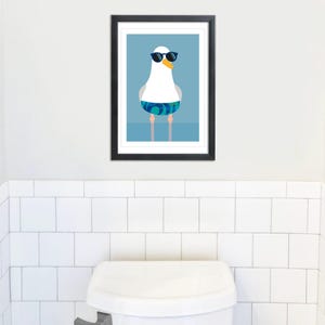 May include: A framed art print depicting a cartoon seagull wearing sunglasses and patterned swim shorts. The seagull has a yellow beak and is set against a light blue backdrop. The artwork is presented in a black frame.