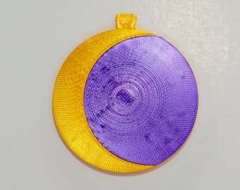 Könnte beinhalten: Zweifarbiges Ornament mit einer goldenen Halbmondform und einem lila kreisförmigen Design. Das Ornament hat oben eine Schlaufe zum Aufhängen. Das Design ist vor einem schlichten, hellgrauen Hintergrund platziert.