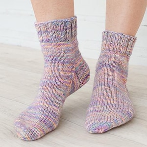 May include: A pair of ankle-length knitted socks featuring a variegated yarn pattern in shades of purple, pink, orange, and blue. The socks have a ribbed cuff at the top and a standard knit construction throughout the foot and heel area.