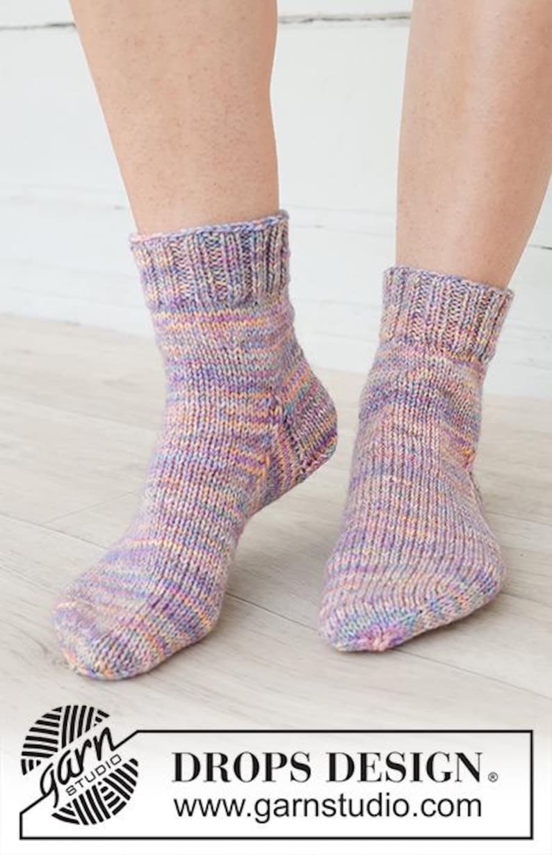 May include: A pair of ankle-length knitted socks featuring a variegated yarn pattern in shades of purple, pink, orange, and blue. The socks have a ribbed cuff at the top and a standard knit construction throughout the foot and heel area.