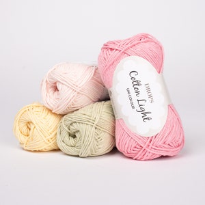 K&ouml;nnte beinhalten: Drei Kn&auml;uel Garn in Rosa, Gelb und Gr&uuml;n. Das rosa Kn&auml;uel hat ein Etikett mit der Aufschrift "DROPS Cotton Light UNI COLOUR".