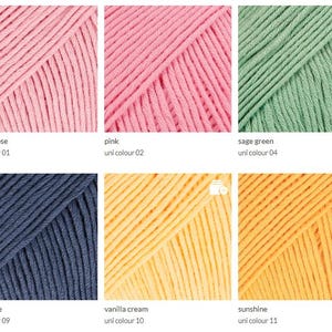 May include: Close-up of six skeins of yarn in various colors: desert rose, pink, sage green, navy blue, vanilla cream, and sunshine. Each skein is labeled with its color name and a uni color number.