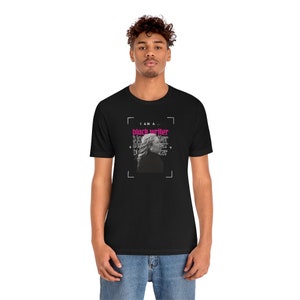 Peut inclure: Un t-shirt noir avec un motif graphique repr&eacute;sentant le visage d'une femme et le texte "I am a... black writer" en rose et noir.