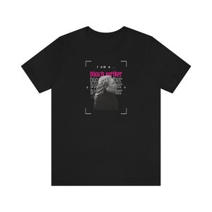 Peut inclure: T-shirt noir avec un graphique d'un visage de femme et le texte "Je suis un... &eacute;crivain noir" en rose.