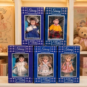 May include: Six vintage Ginny dolls in their original blue boxes. Each doll is in a different outfit, with details like a white dress, a yellow shirt, and a plaid skirt. The boxes are labeled "Ginny" and "Vogue Dolls."