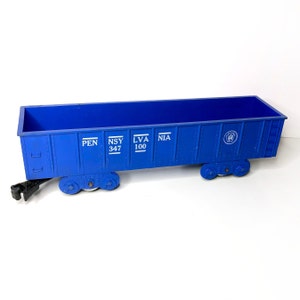 May include: Blue toy train car with the words "PEN", "NSY 347", "LVA 100", and "NIA" printed on the side. The car has a black metal coupler and four black wheels.