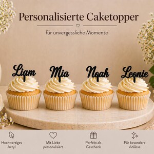 Könnte beinhalten: Vier Cupcakes mit weißem Zuckerguss und personalisierten schwarzen Tortenaufsätzen mit den Namen "Liam", "Mia", "Noah" und "Leonie". Die Cupcakes stehen auf einer runden, hellen Oberfläche, mit Blumen und Text im Hintergrund.