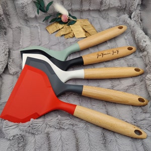 Könnte beinhalten: Vier Silikon-Spatel mit Holzgriffen. Die Spatel sind rot, grau, weiß und grün. Die Holzgriffe sind mit dem Text "Jazmin Joy" graviert.