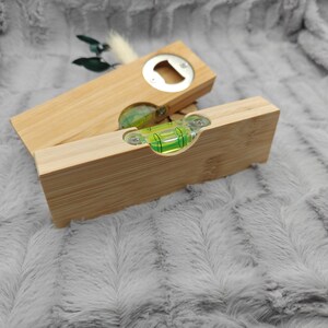 May include: A wooden bottle opener and a level tool. The bottle opener is rectangular with a silver opener. The level tool is also rectangular with a green bubble level. Both are made of light-colored wood.