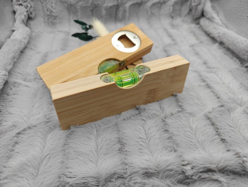 May include: A wooden bottle opener and a level tool. The bottle opener is rectangular with a silver opener. The level tool is also rectangular with a green bubble level. Both are made of light-colored wood.
