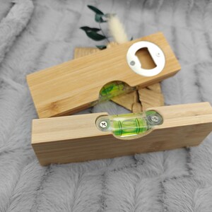 May include: Two wooden bottle openers with a level built in. One opener is on top of the other. The openers are made of light-colored wood and have a silver bottle opener on one end. The level is visible through a clear window.