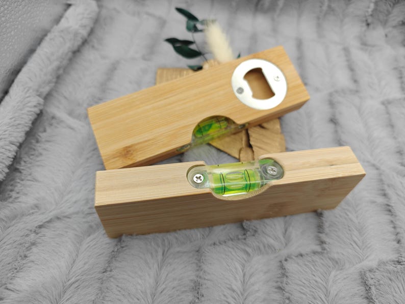 May include: Two wooden bottle openers with a level built in. One opener is on top of the other. The openers are made of light-colored wood and have a silver bottle opener on one end. The level is visible through a clear window.