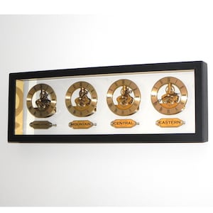 May include: A black framed wall clock with four gold-toned clock faces displaying different time zones: Pacific, Mountain, Central, and Eastern.
