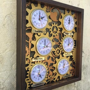 May include: A wooden wall clock with a gold gear design and five clocks showing different time zones: Pacific, Mountain, Eastern, Central, and Hawaii. The clocks are labeled with their respective time zones.