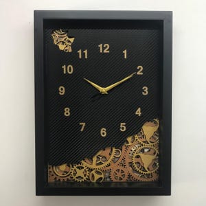 May include: Black framed wall clock with gold gears and Roman numeral hour markers. The clock face is black with a carbon fiber pattern.