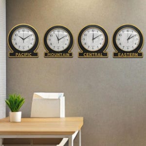 Può includere: Quattro orologi rotondi con cornici nere e dettagli dorati, ognuno che mostra un fuso orario diverso: Pacifico, Montagna, Centrale ed Est.