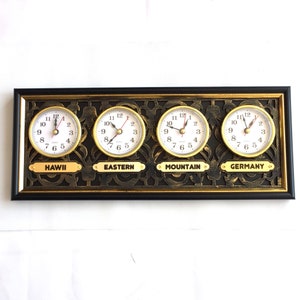 May include: A black framed wall clock with four gold-rimmed clock faces displaying different time zones: Hawaii, Eastern, Mountain, and Germany.