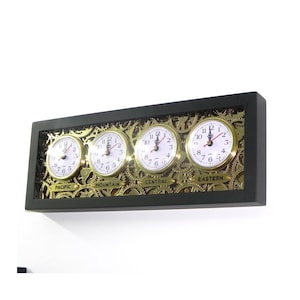 May include: A black framed wall clock with three gold-toned clock faces displaying different time zones: Pacific, Mountain, and Eastern. Each clock face has a white background with black numbers and hands.