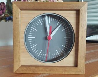 Puede incluir: Un reloj de madera con una esfera gris y agujas blancas. El reloj tiene una aguja de segundos roja.