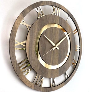 May include: A large, round, wooden wall clock with Roman numeral markings and gold-coloured hands. The clock face has a gold-coloured ring around the centre.