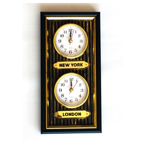 Puede incluir: Un reloj enmarcado en negro con detalles dorados muestra dos relojes, uno para Nueva York y otro para Londres. Los relojes tienen esferas blancas con números y manecillas negras.
