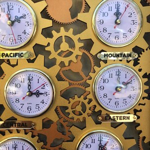 May include: A gold-colored wall clock with four round analog clocks displaying different time zones. The clocks are labeled "Pacific", "Mountain", "Central", and "Eastern".