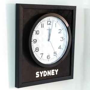 Puede incluir: Un reloj enmarcado en negro con agujas y números blancos. La esfera del reloj dice "GALAXY" y "SYDNEY".