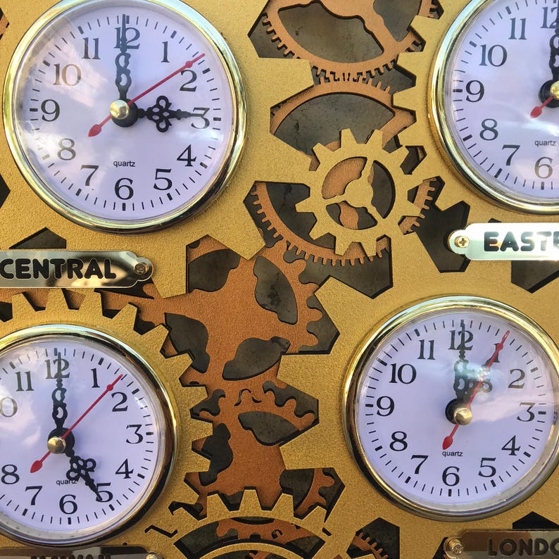 May include: A gold-colored wall clock with four round analog clocks, each with a different time zone: Central, Eastern, London, and a fourth time zone. The clocks are connected by gears and have a gold-colored background.