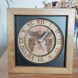 May include: A wooden clock with a black frame and a round face. The face has Roman numerals and a design of an eagle with American flags. The clock hands are red and silver.