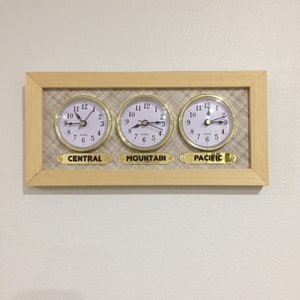Könnte beinhalten: Eine Wanduhr in einem Holzrahmen mit drei runden analogen Uhren, die verschiedene Zeitzonen anzeigen: Central, Mountain und Pacific.