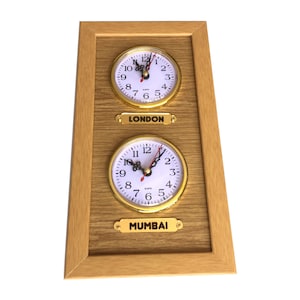 May include: A wooden framed clock with two round analog clocks. The top clock is labeled "LONDON" and the bottom clock is labeled "MUMBAI".