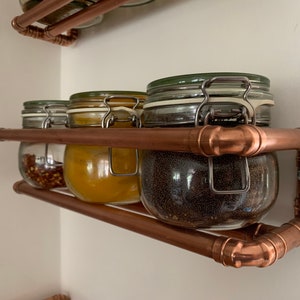 May include: Copper pipe spice rack with four glass jars filled with spices. The jars have metal lids with clips.