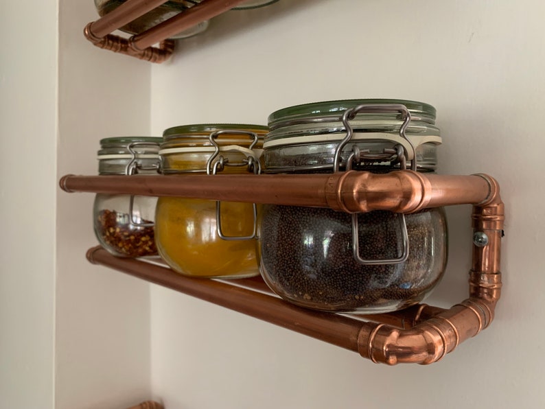 May include: Copper pipe spice rack with four glass jars filled with spices. The jars have metal lids with clips.