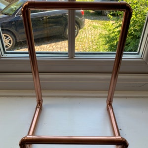 May include: A copper pipe stand for displaying books or other items. The stand is made of copper pipe and has a simple, modern design.