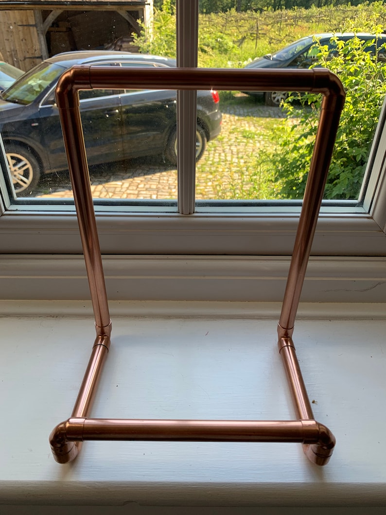 May include: A copper pipe stand for displaying books or other items. The stand is made of copper pipe and has a simple, modern design.
