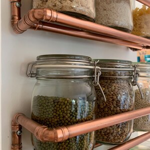 May include: Copper pipe shelving unit with glass jars filled with various dried goods, including rice, lentils, and mung beans.